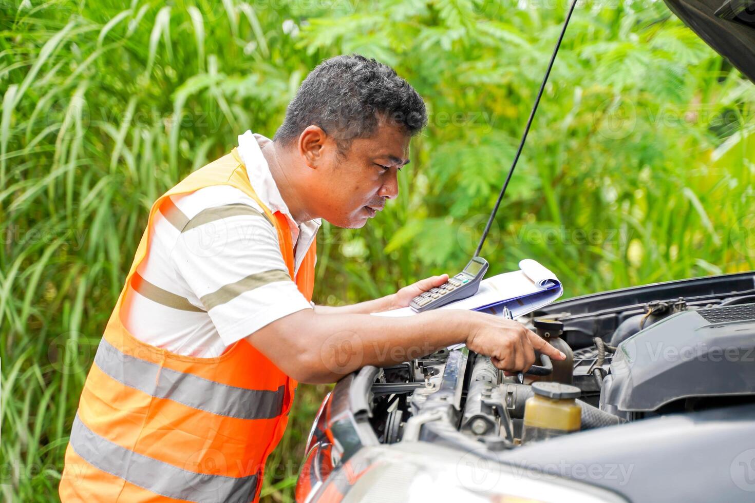 Car mechanic performs basic engine check and carrying a clipboard and a cost estimate for repairs from an engine breakdown photo