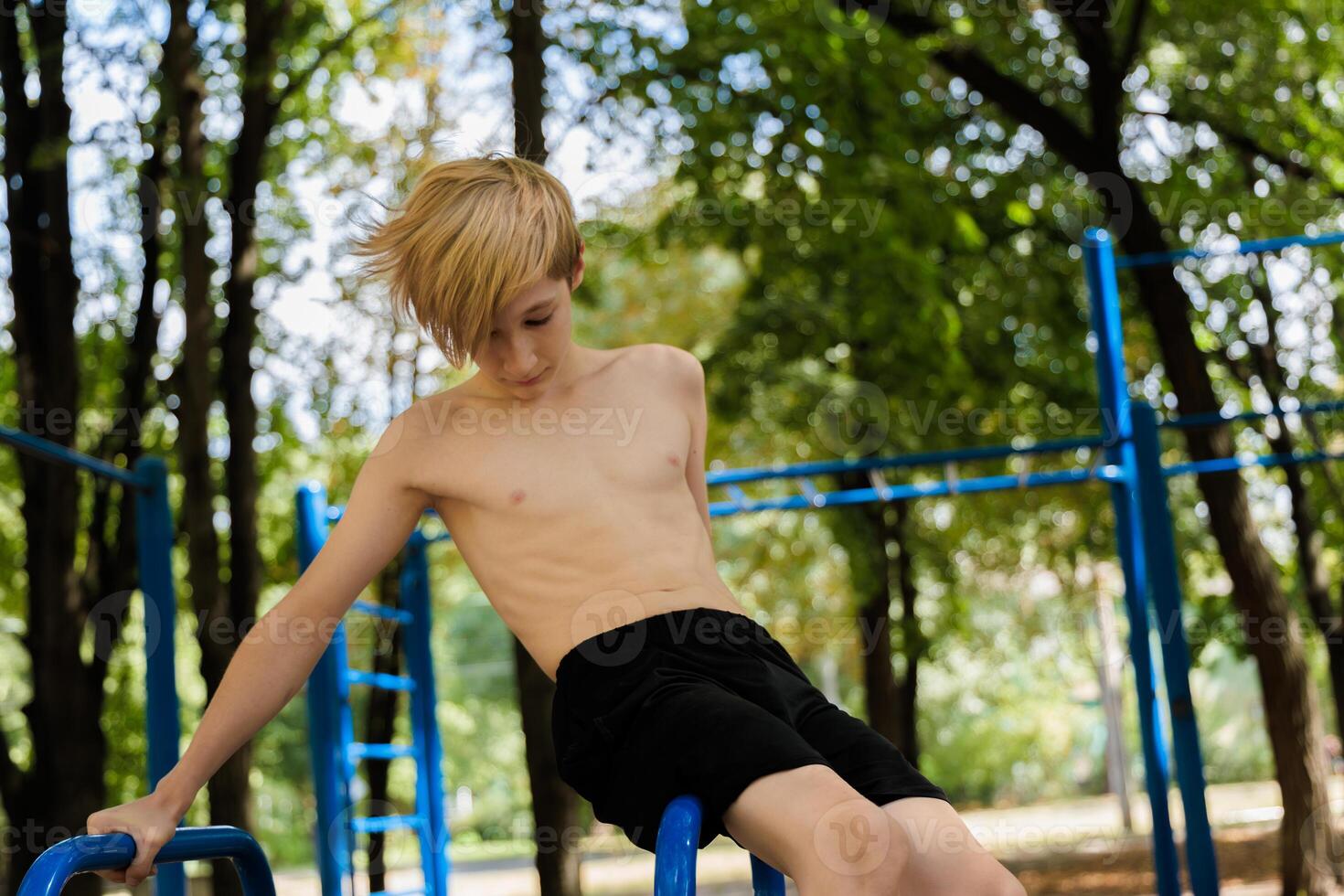 Athletic boy sitting on a projectile looking down with his legs overhanging. Athletic teenage boy in the park outdoor workout session photo