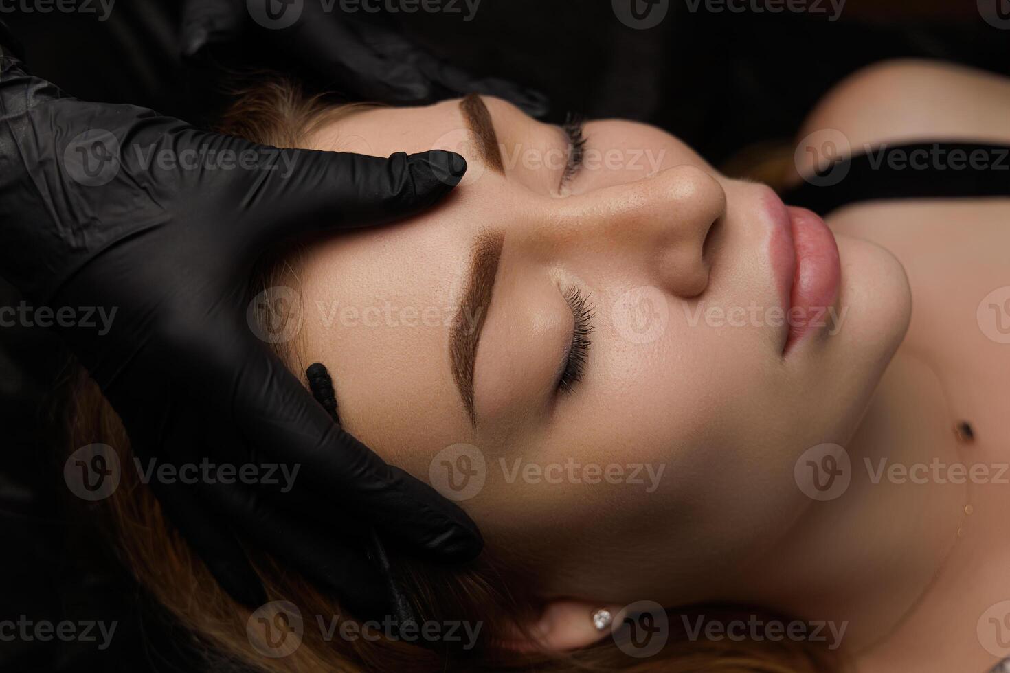Beautiful permanent eyebrow makeup work for a young girl who is lying relaxed with her eyes closed Permanent eyebrow makeup, eyebrow tattooing with brown pigment for PMU. photo