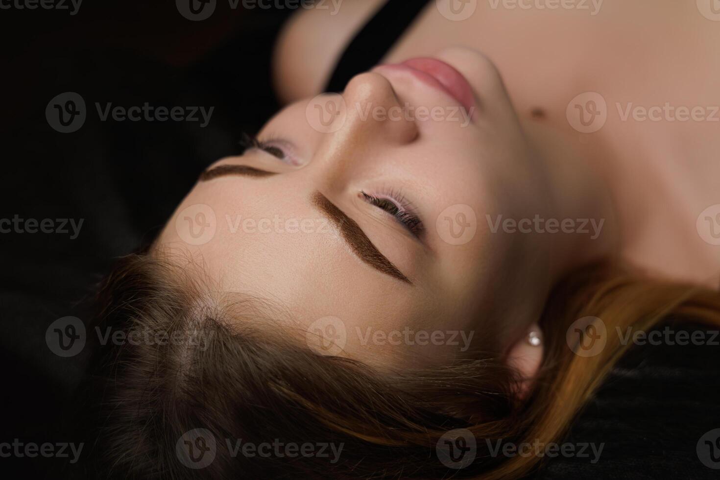 Beautiful eyebrows after permanent eyebrow makeup girl lying dark cosmetology salon Permanent eyebrow makeup, eyebrow tattooing with brown pigment for PMU. photo
