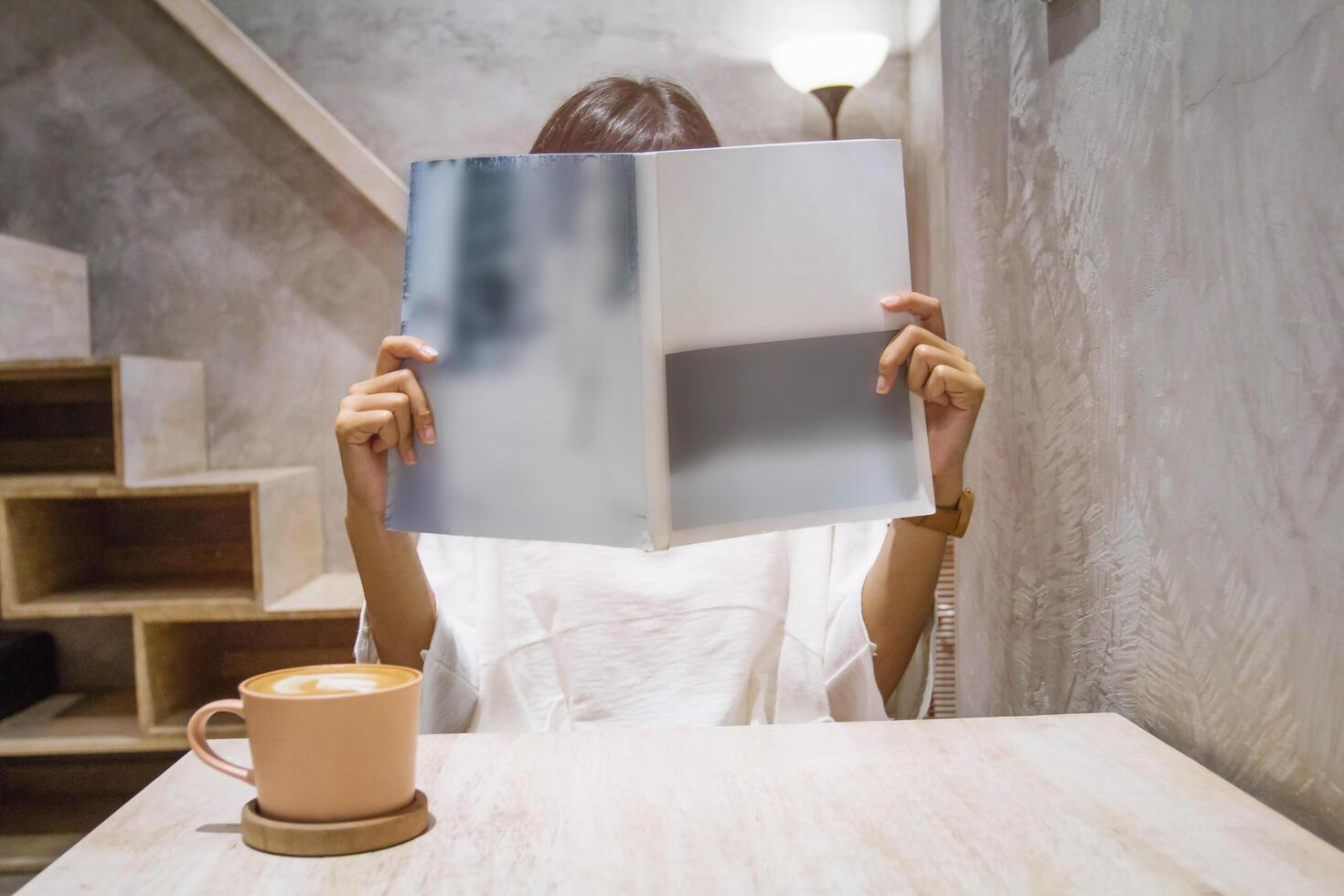 Close up and selective focus woman reading book or magazine with drinking coffee at cafe. photo