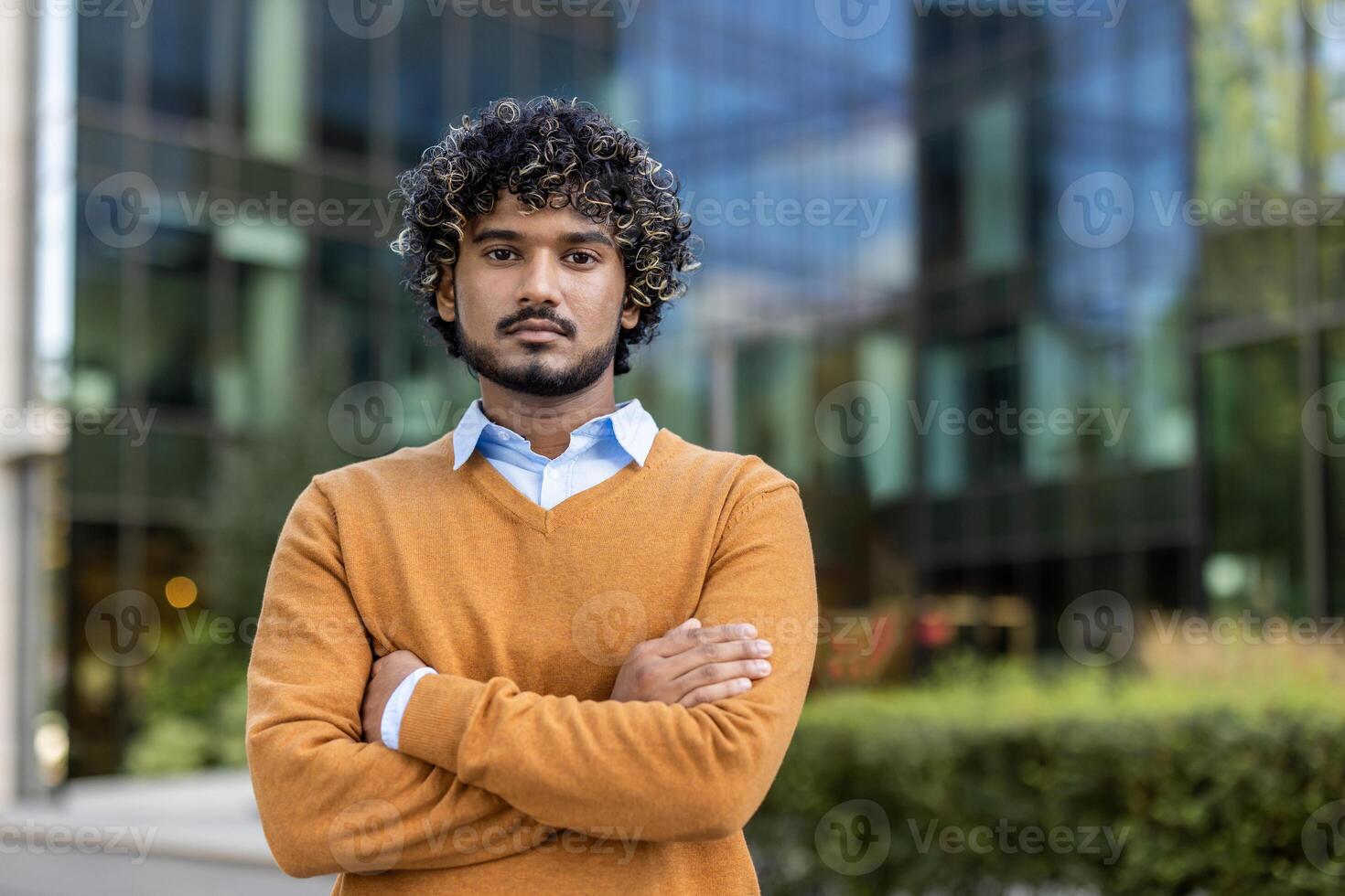 Confident Indian businessman standing with arms crossed in front of modern office building. Man expressing professionalism and confidence. Suitable for themes of leadership, business, and modern work photo