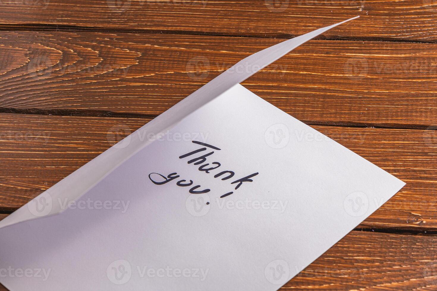 Half open sheet of paper with the words thank you on a brown wooden table photo