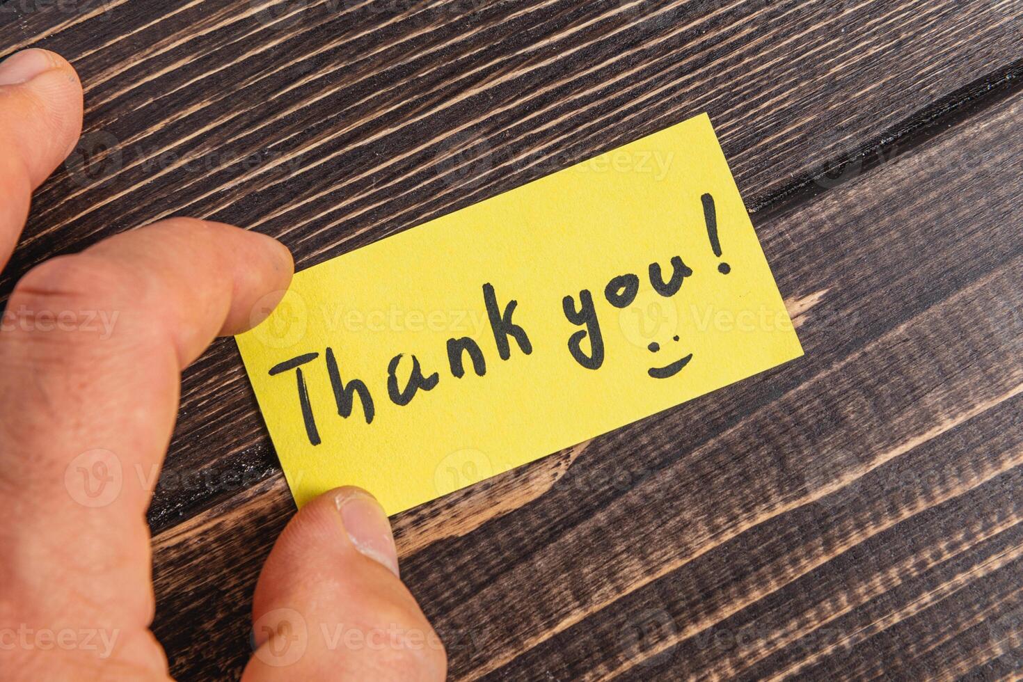 A note with the word thank you in the hand of a man on the table photo