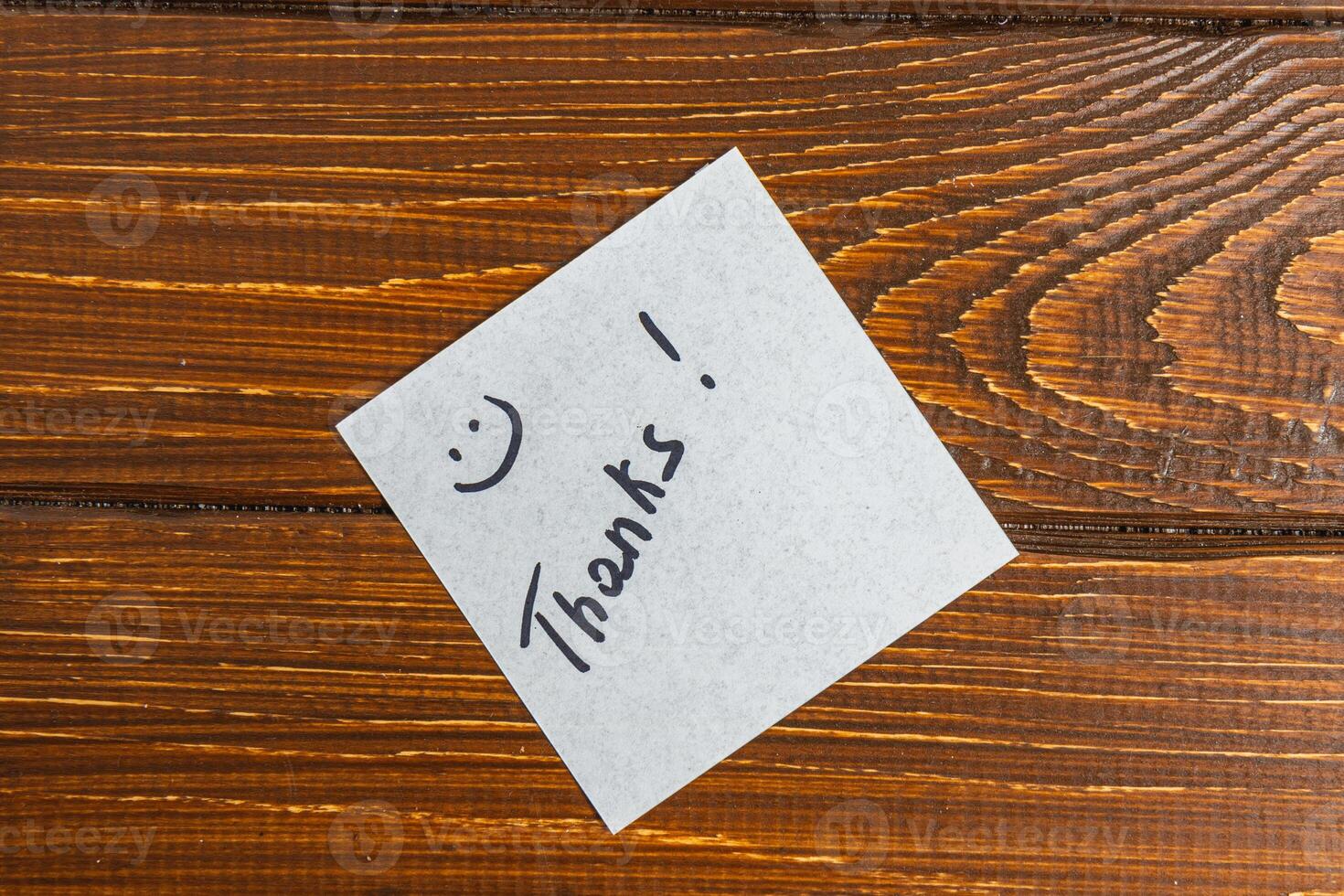 A thank you note is written on a piece of paper and placed on a wooden surface. photo