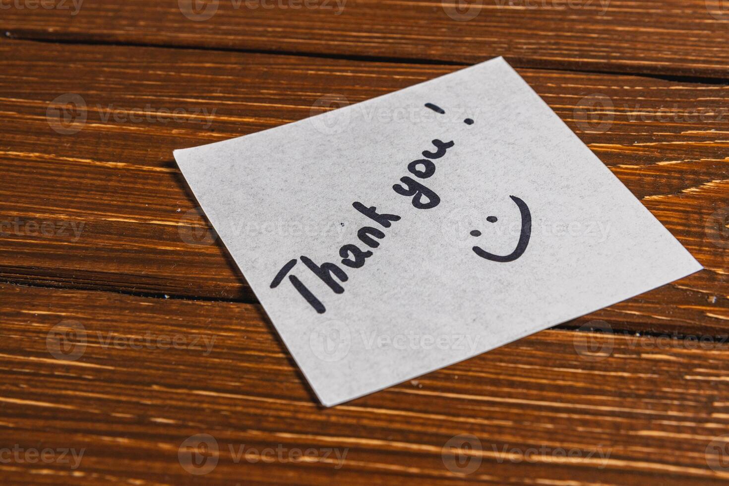 A thank you note is written on a piece of paper and placed on a wooden surface. photo
