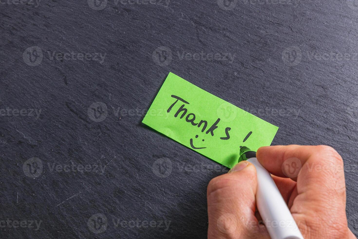 A man writes the word thank you on a small green piece of paper on a table photo
