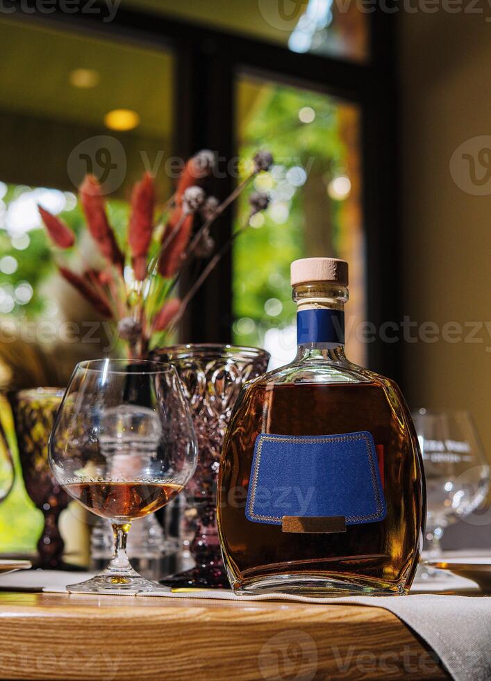 Bottle of cognac and glass are sitting on table in restaurant photo