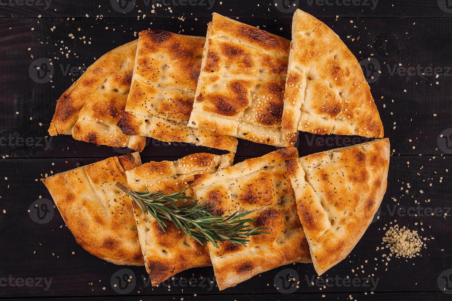 Sliced pide bread sprinkled with sesame seeds and rosemary on dark wooden table photo