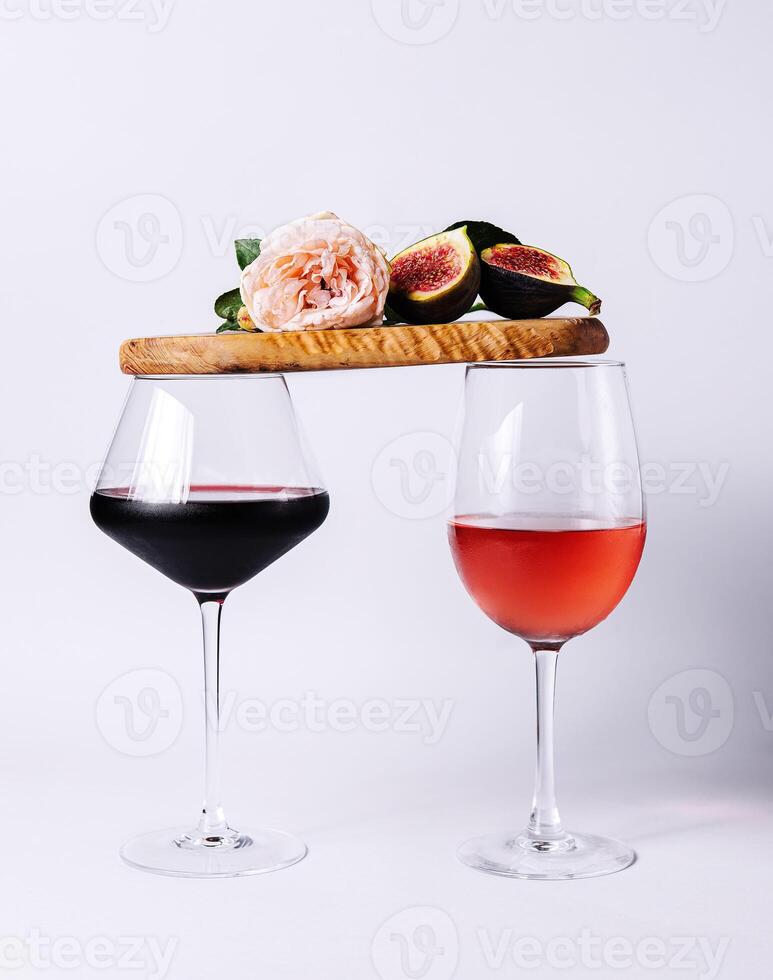 Two glasses with red and rose wine balancing wooden board with ripe figs and pink rose photo