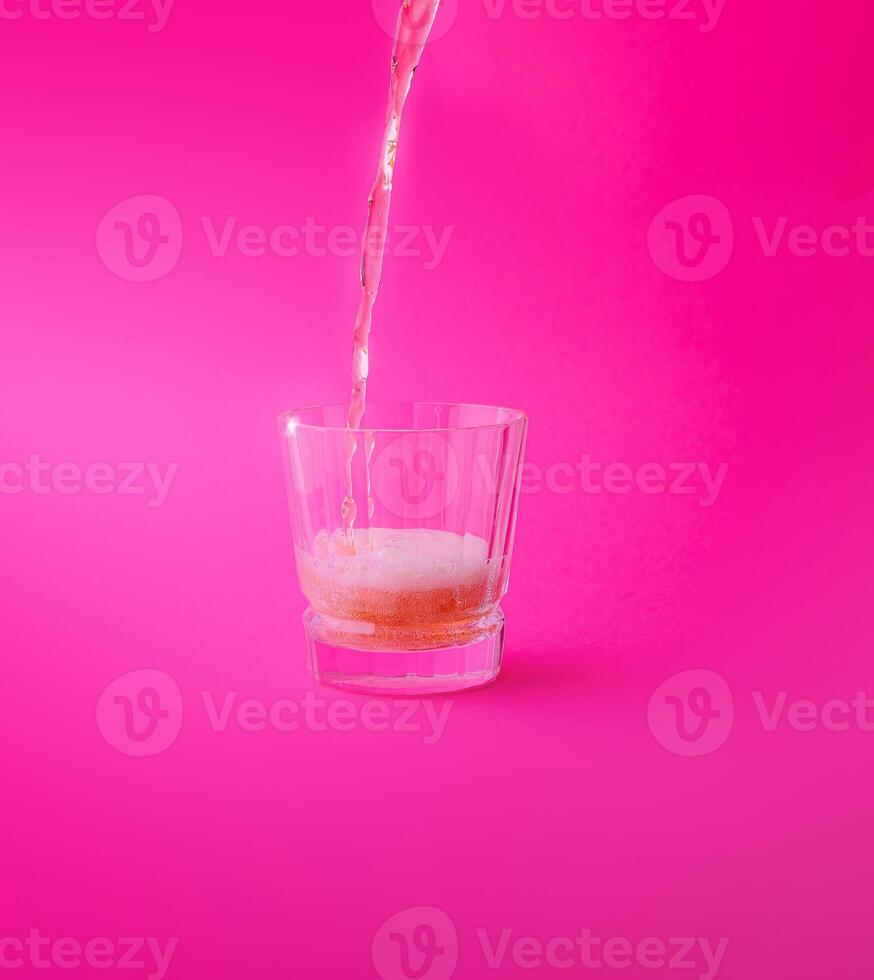 Pink drink being poured into a glass on a pink background photo