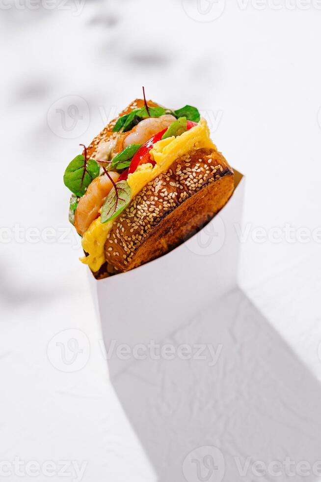 Delicious toasted sandwich with shrimps, scrambled eggs and salad in a white cardboard box for delivery photo