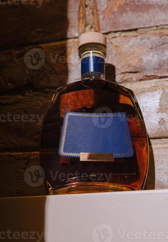 Bottle of cognac sitting on shelf with blank label and brick background photo