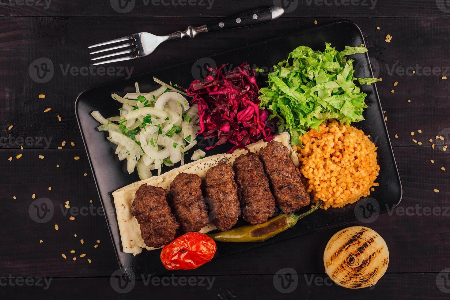 Delicious kofta kebabs served on pita bread with spices and vegetables on black plate photo