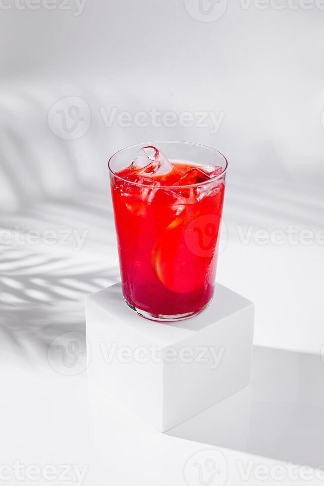 Refreshing red cocktail standing on white cube with tropical palm leaf shadow photo