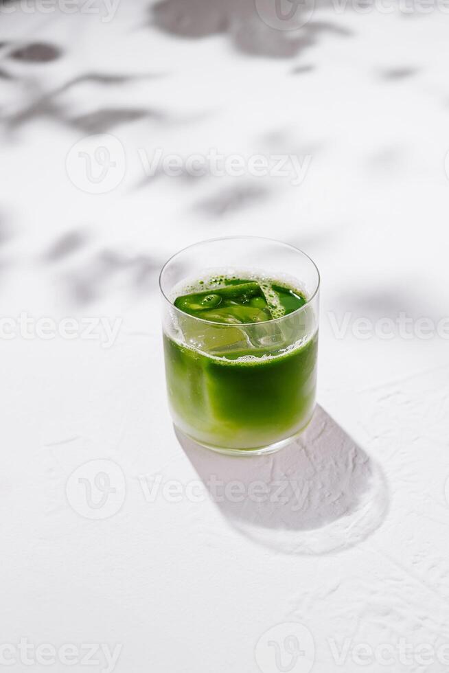 Green iced matcha latte standing on white table with leaf shadows photo