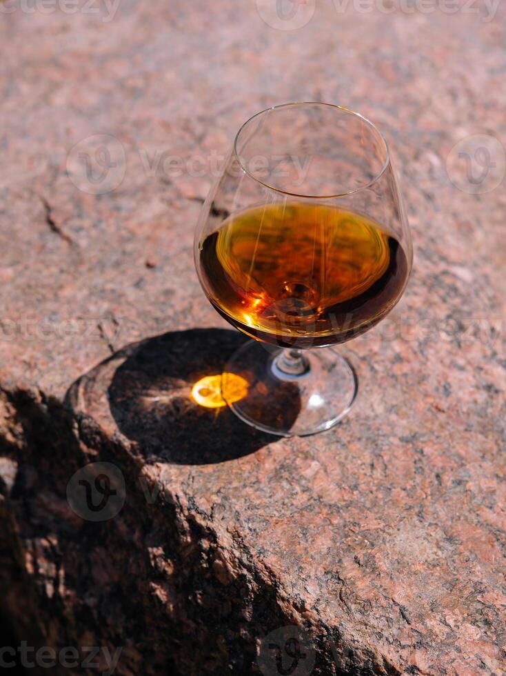 Glass of cognac standing on a rock in the sunlight photo