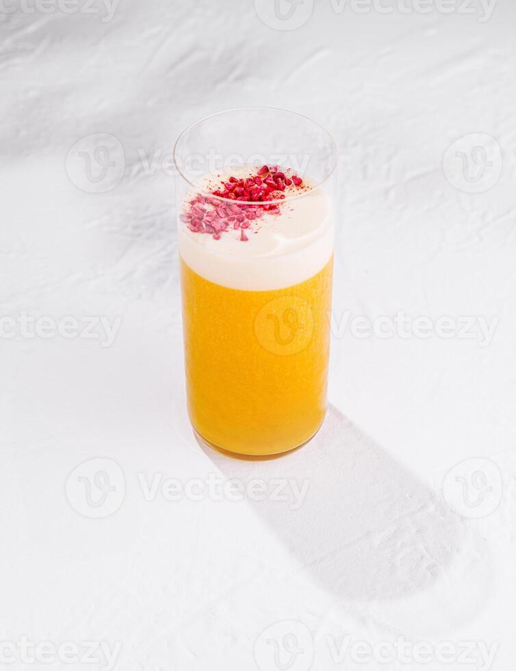 Refreshing yellow cocktail with white foam and raspberry powder topping on white background photo