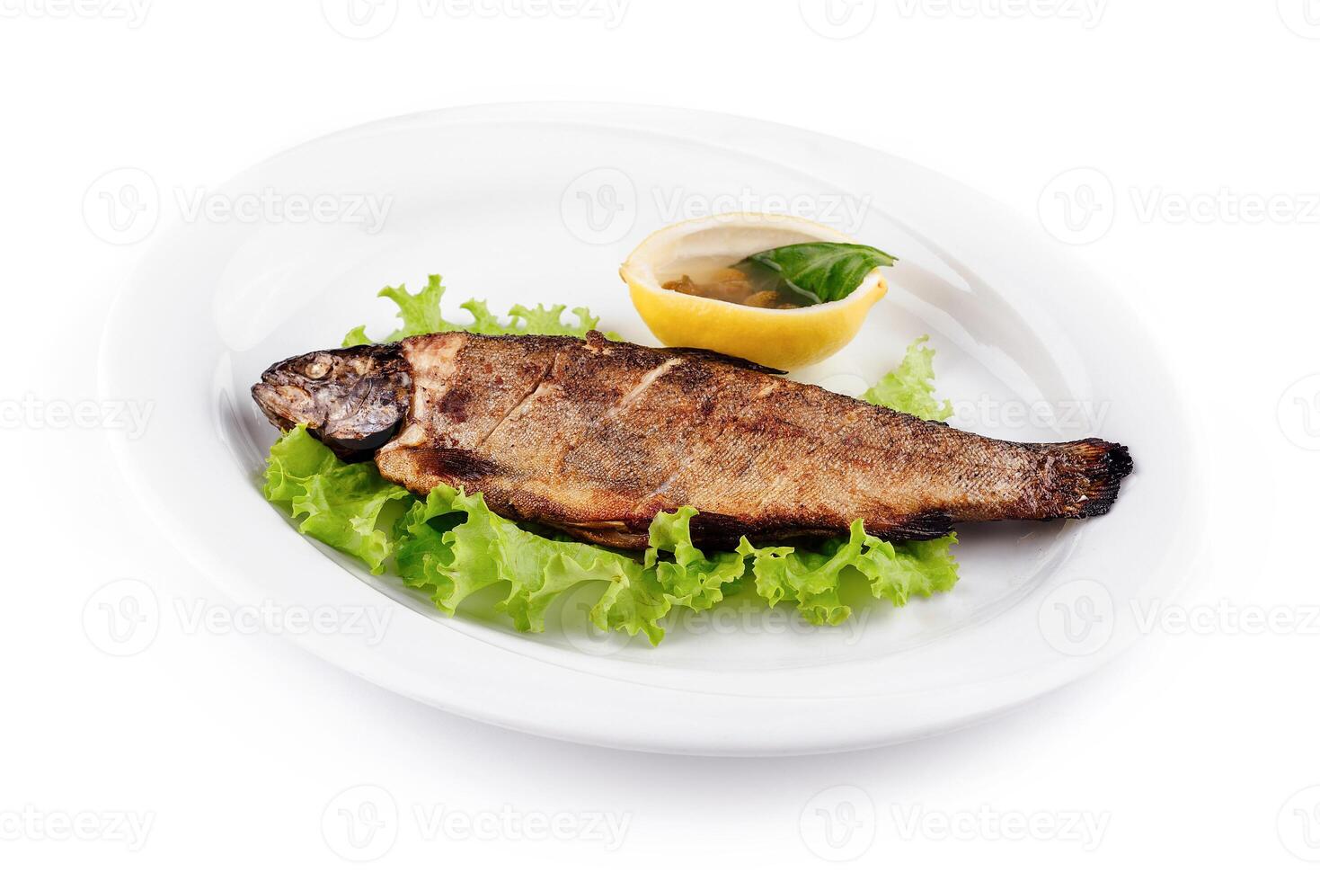 Grilled trout served on bed of lettuce with lemon and condiment photo
