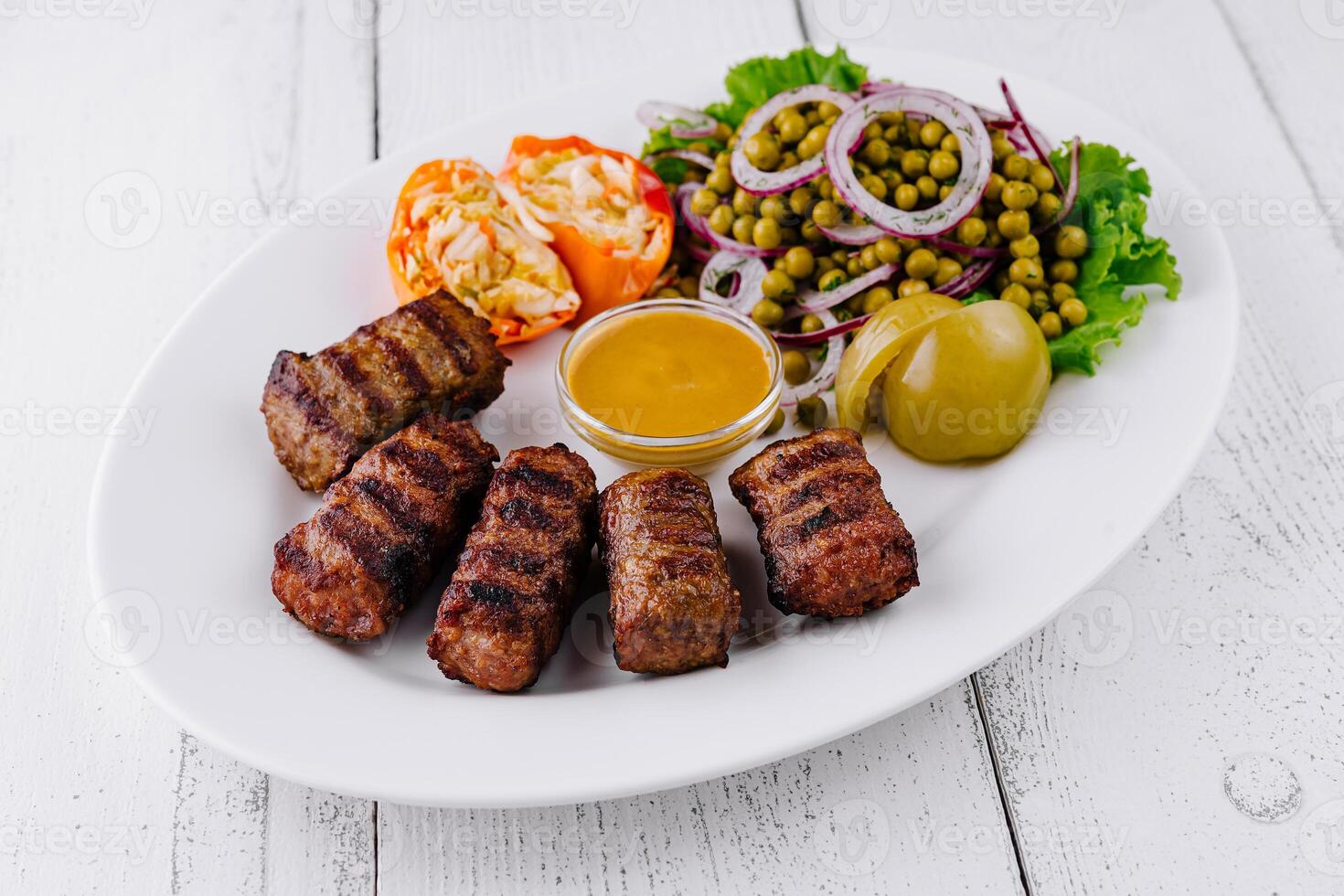 Grilled minced meat kebab with mustard, pickles, and green pea salad on white plate photo