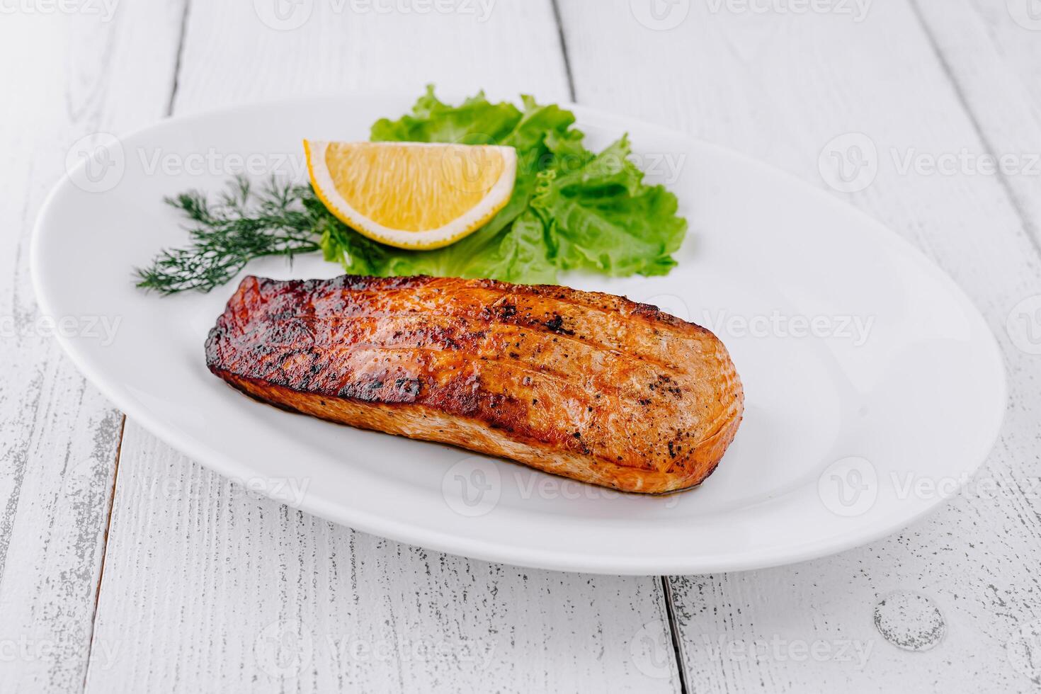Grilled salmon steak lying on white plate with lemon and lettuce photo