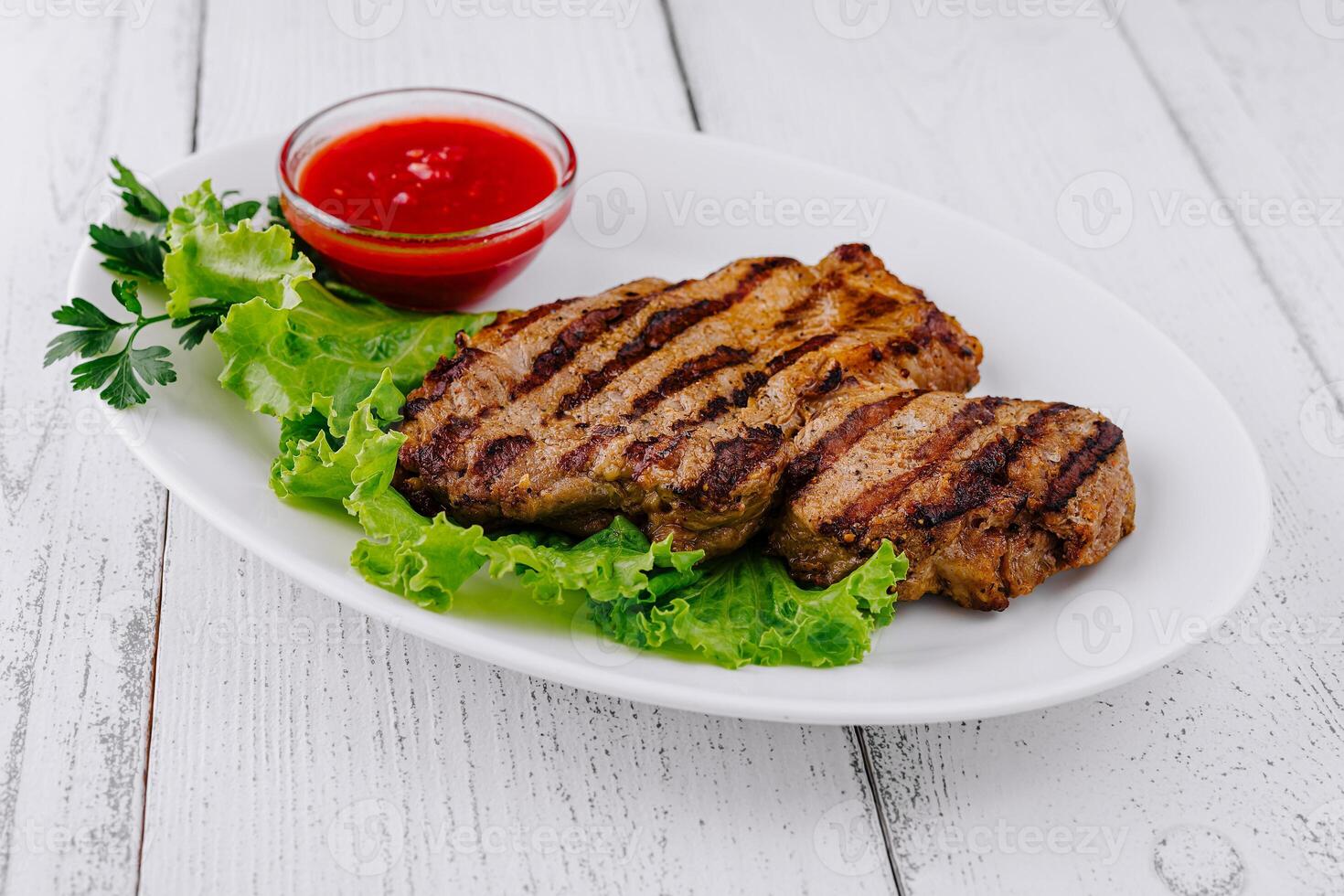 Grilled steak lying on fresh lettuce with tomato sauce on white plate photo