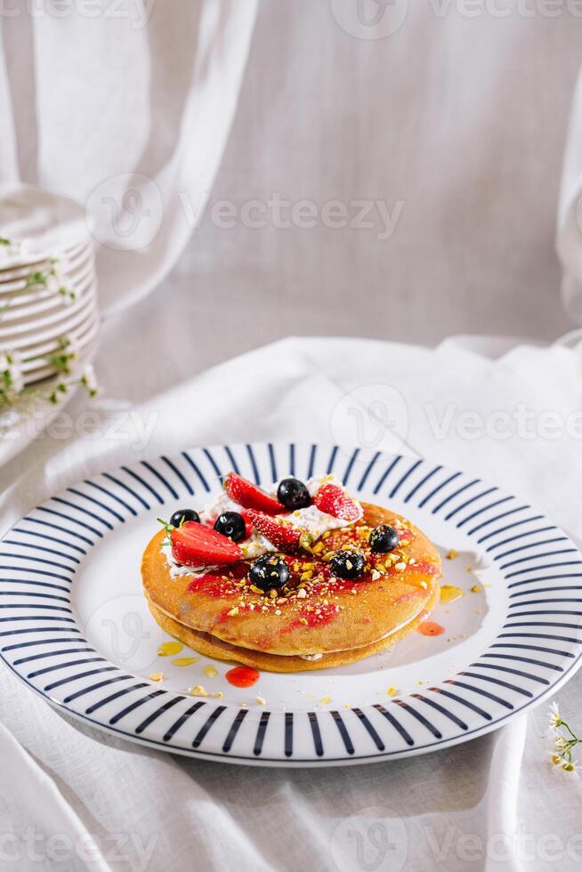 Stack of pancakes lying on plate with blue stripes, topped with strawberries, blueberries and pistachios photo