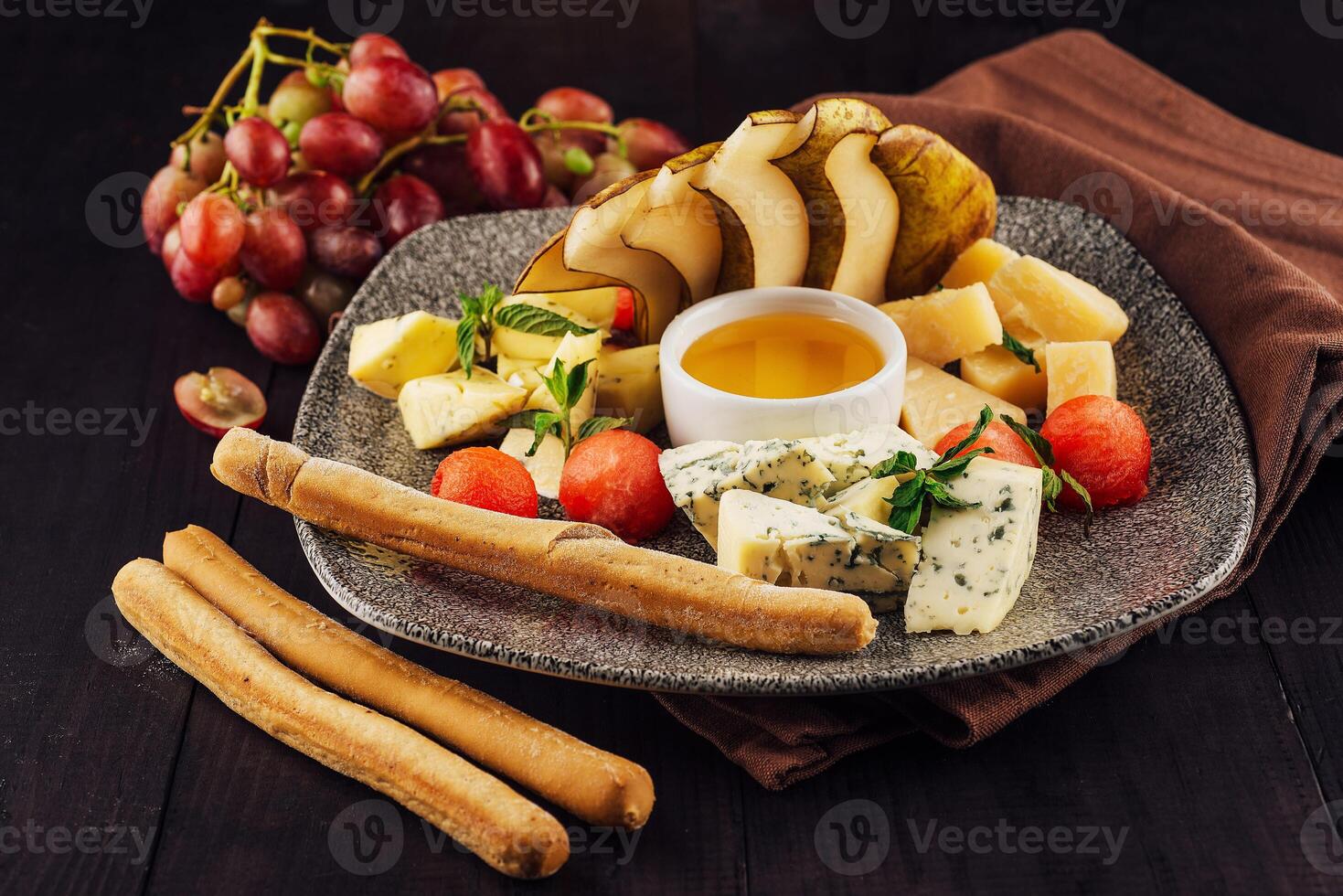 Gourmet cheese plate offering variety of textures and flavors with honey and grapes photo