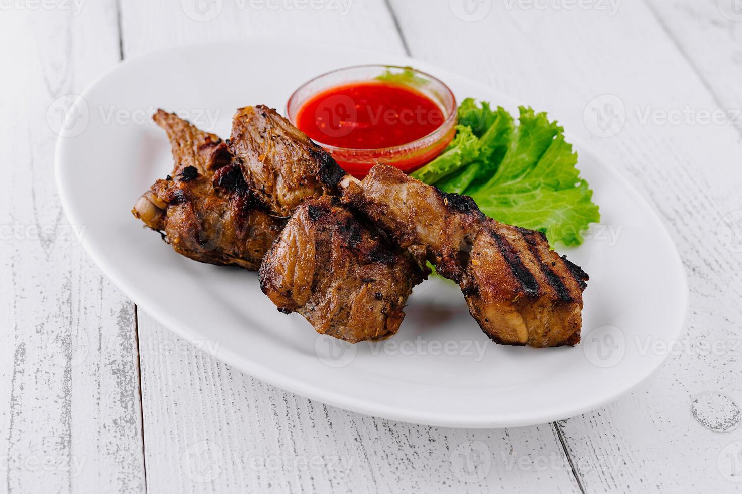 Grilled lamb chops served on white plate with spicy tomato sauce and salad photo