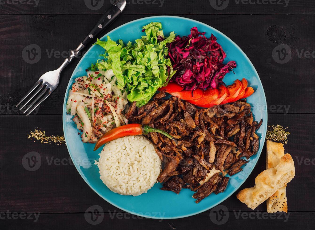 Delicious iskender kebab is served on a blue plate with rice, fresh vegetables and pita bread photo