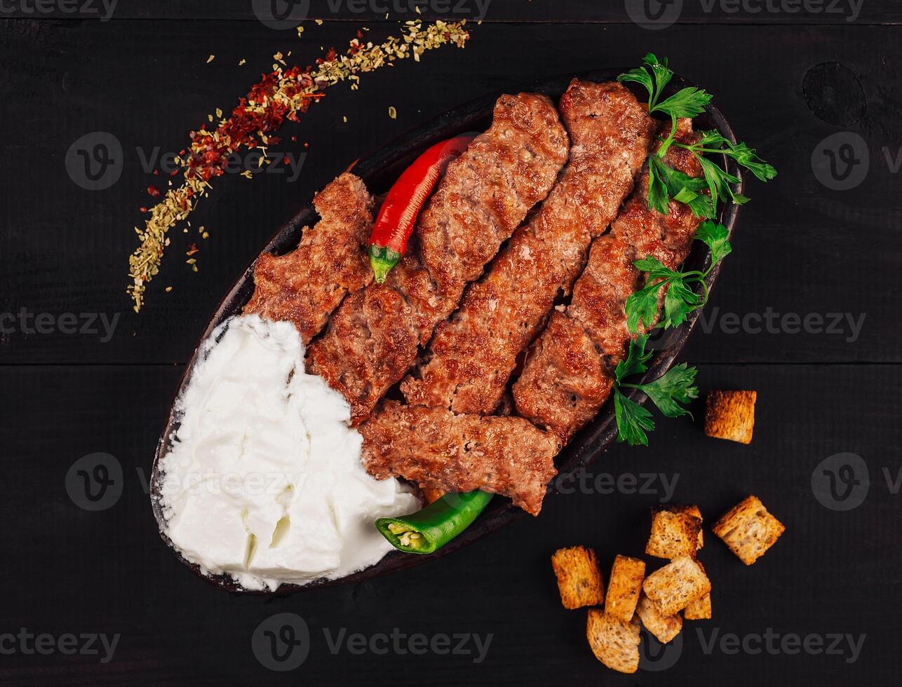 Spicy lule kebab served on a traditional plate with yogurt and croutons photo