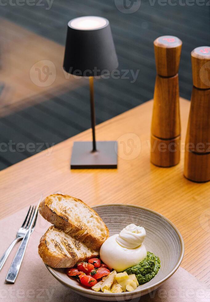 Delicious burrata salad served on restaurant table with toasted bread slices photo