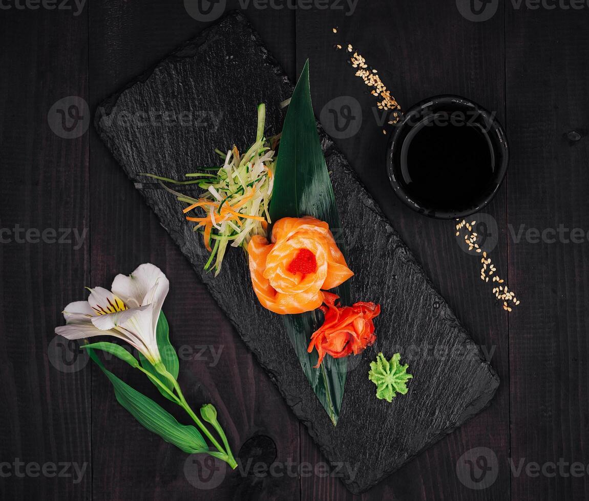 Salmon sashimi rose served on slate with wasabi and ginger on dark wooden table photo