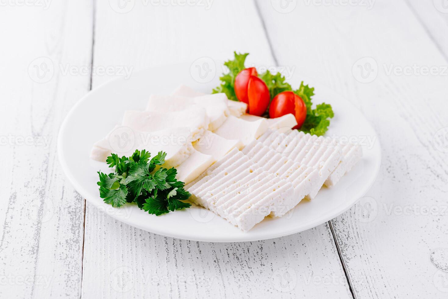 White cheese slices with cherry tomatoes and parsley on white plate photo