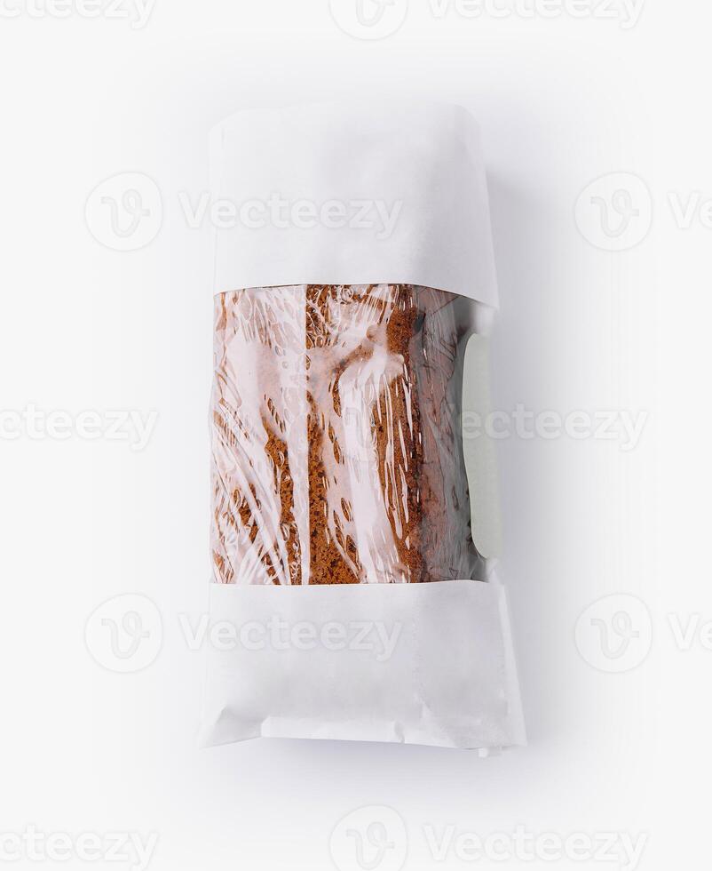 Freshly baked banana bread wrapped in plastic and paper bag on white background photo