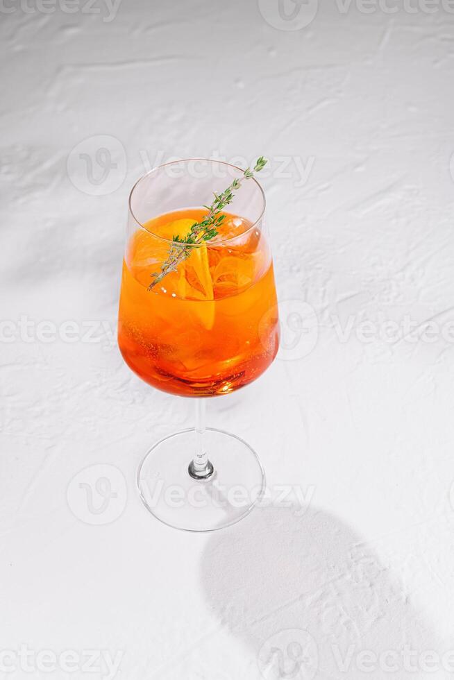 Aperol spritz cocktail standing on white table with thyme garnish photo