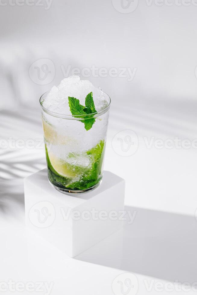 Refreshing mojito cocktail standing on white cube with tropical palm leaf shadow photo