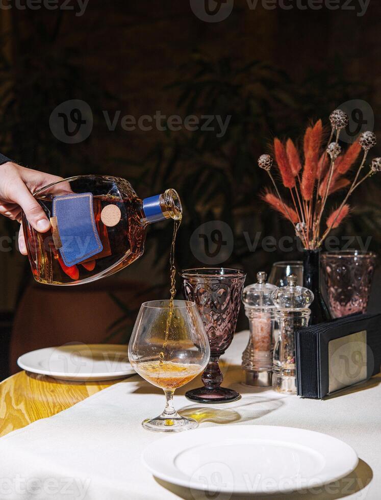 Waiter pouring cognac into glass on restaurant table photo
