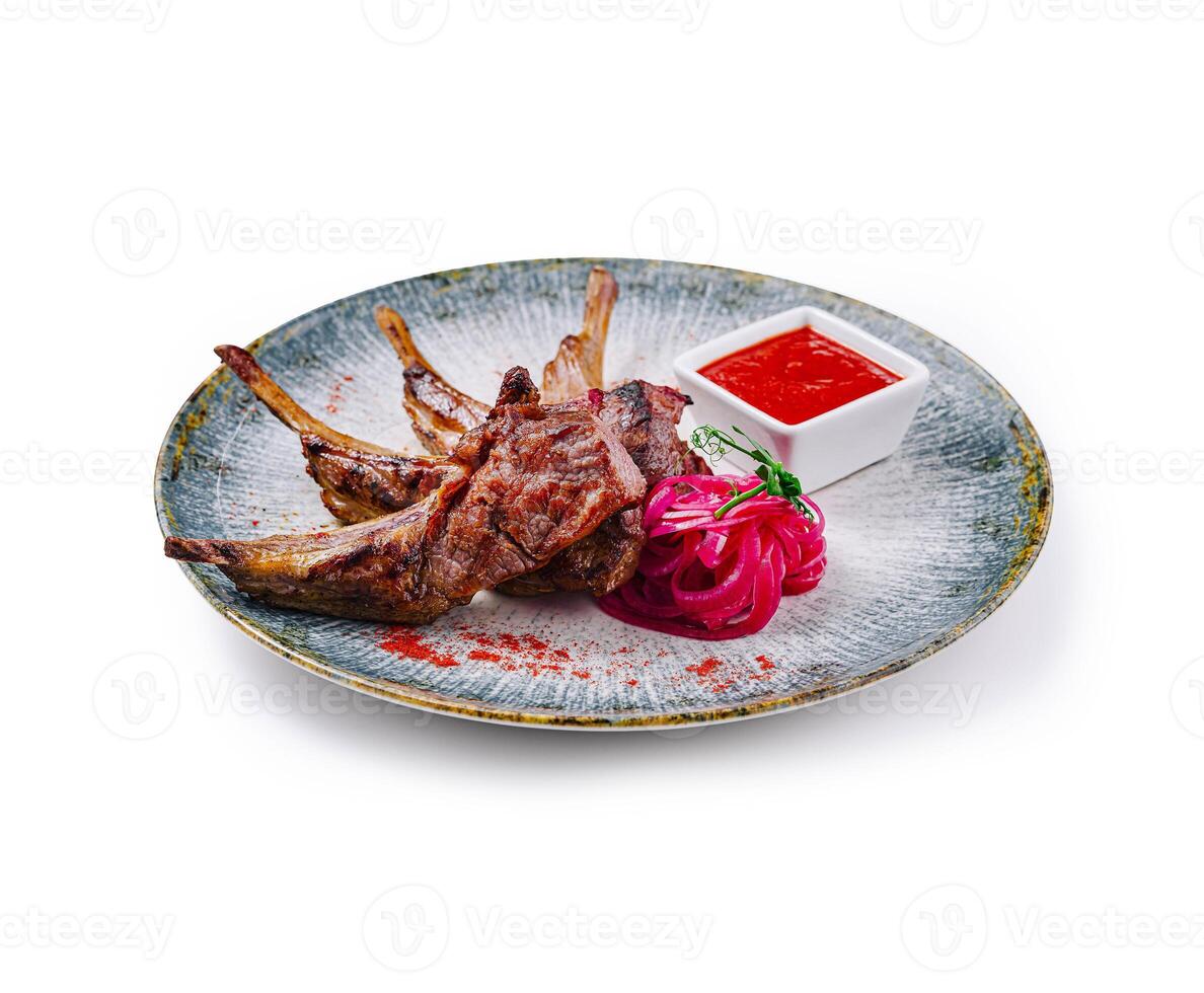 Grilled lamb ribs with red sauce, onion and herbs on plate photo