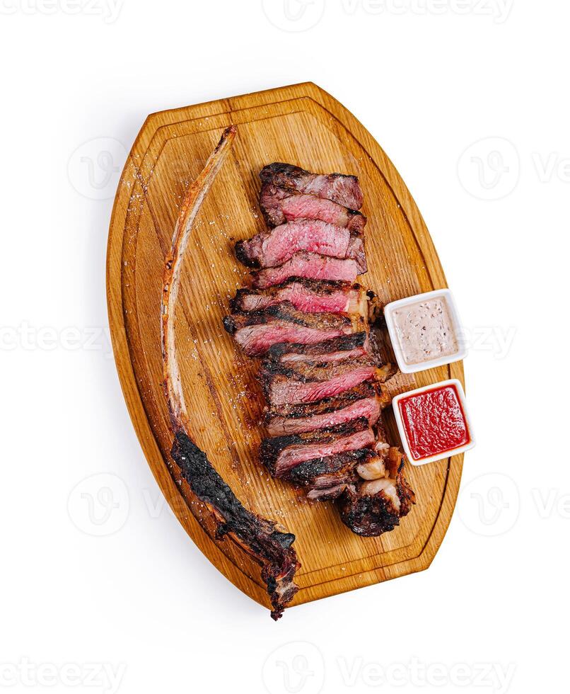 Grilled tomahawk steak lying on wooden board with sauces photo