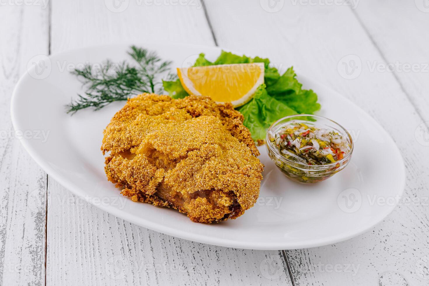 Breaded fish fillet served on white plate with lemon and sauce photo