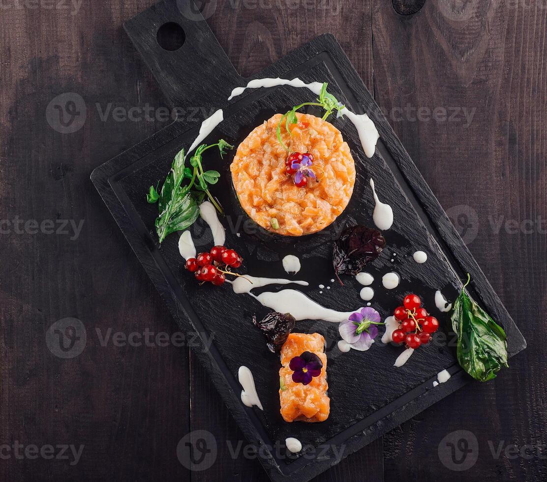 Salmon tartare garnished with flowers and redcurrant resting on black slate plate photo