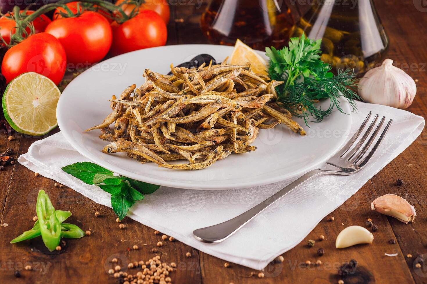 Fried anchovies served on white plate with herbs and spices on rustic wooden table photo