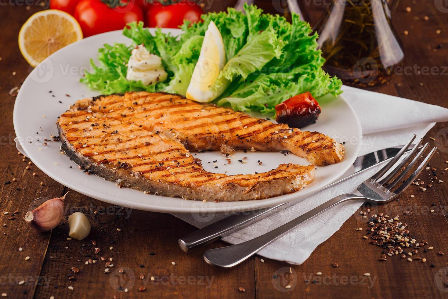 Grilled salmon steak with lettuce and lemon on white plate photo