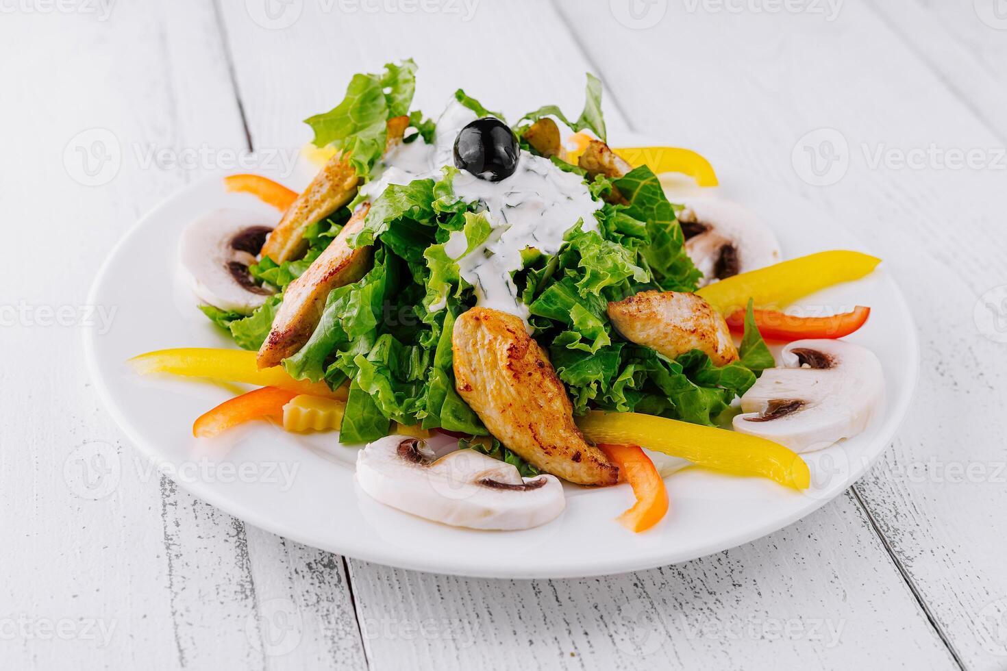 Delicious salad with grilled chicken, mushrooms and yogurt dressing on white wooden table photo