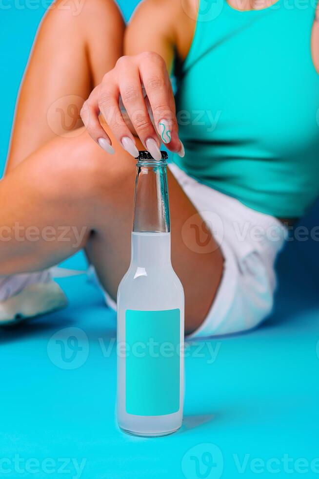 Woman opening bottle of refreshing cold drink with blank label on blue background photo