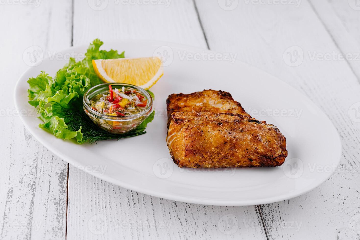 Grilled salmon fillet served on white plate with lemon and sauce photo