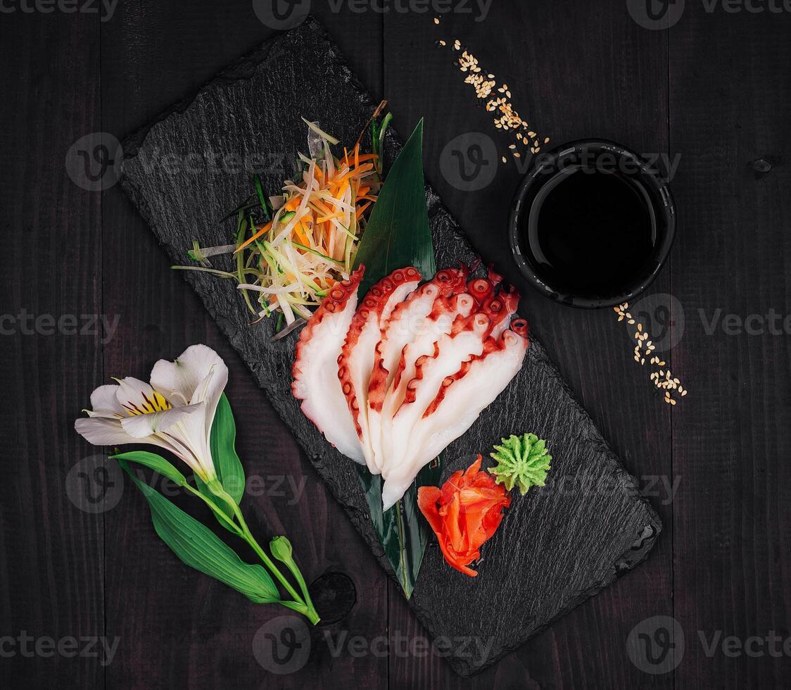 Sliced octopus sashimi with soy sauce and wasabi on slate serving board photo