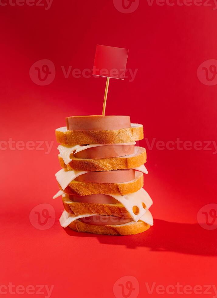 Big tower made of bread, sausage and cheese with blank red flag on the top standing on red background photo