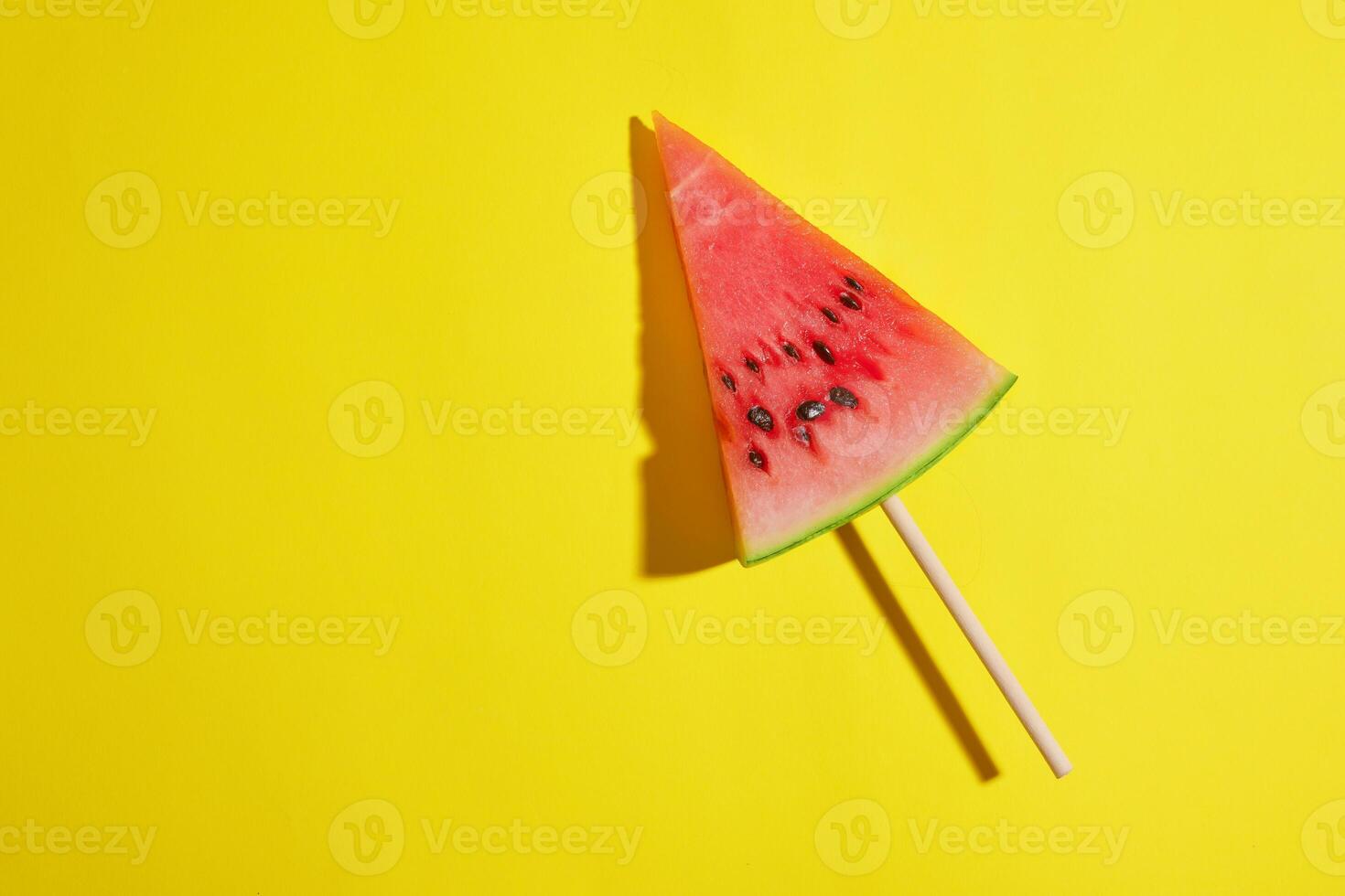 triangular piece of watermelon on a stick on a yellow background photo